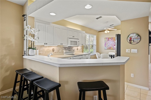 kitchen featuring white appliances, a breakfast bar area, tasteful backsplash, white cabinets, and kitchen peninsula