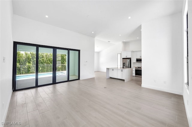 unfurnished living room with light hardwood / wood-style floors, a towering ceiling, and french doors