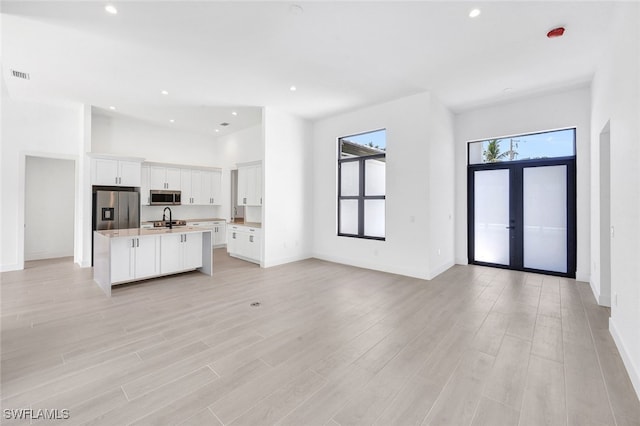 kitchen featuring light wood-type flooring, french doors, a kitchen island with sink, white cabinetry, and stainless steel appliances