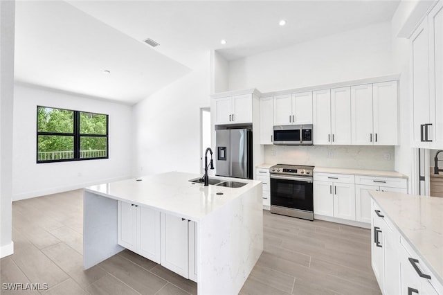 kitchen with tasteful backsplash, a kitchen island with sink, white cabinets, appliances with stainless steel finishes, and light stone countertops