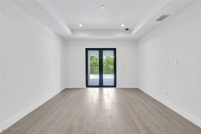 unfurnished room with french doors, light hardwood / wood-style floors, and a tray ceiling