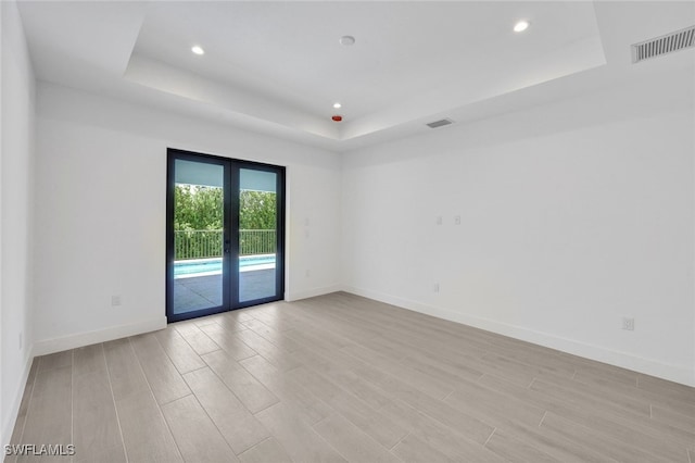 empty room featuring a raised ceiling, french doors, and light hardwood / wood-style floors