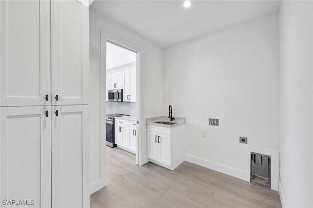 clothes washing area with sink, light hardwood / wood-style flooring, electric dryer hookup, and cabinets