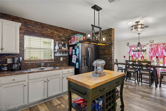 kitchen with sink, light hardwood / wood-style floors, stainless steel refrigerator with ice dispenser, hanging light fixtures, and white cabinets