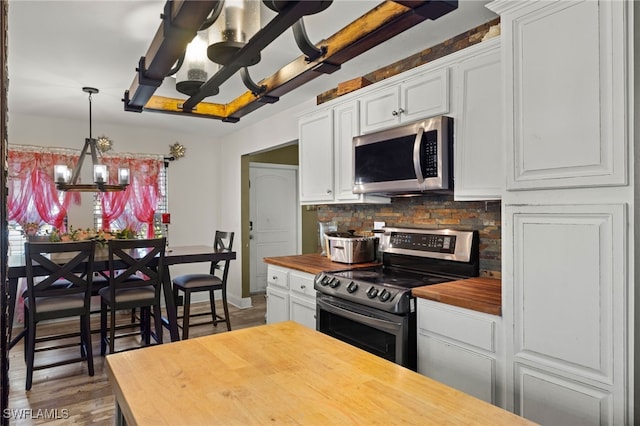 kitchen with butcher block countertops, hardwood / wood-style floors, white cabinetry, an inviting chandelier, and stainless steel appliances