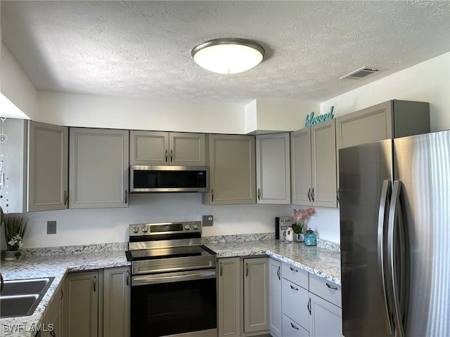 kitchen with light stone countertops, gray cabinets, a textured ceiling, and appliances with stainless steel finishes