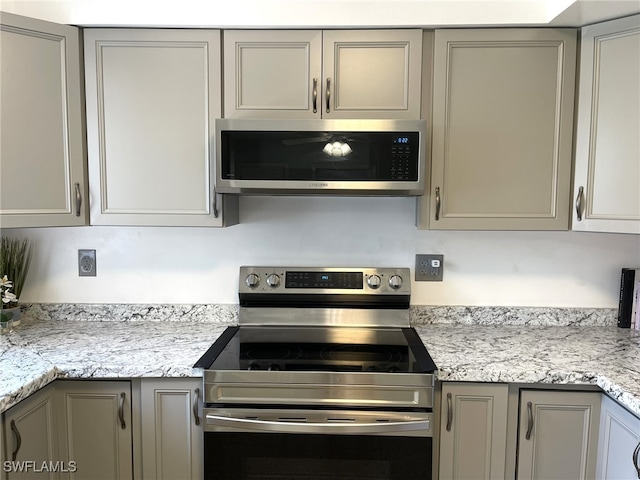 kitchen with stainless steel appliances, gray cabinets, and light stone countertops