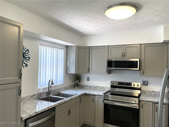 kitchen featuring light stone countertops, a textured ceiling, stainless steel appliances, gray cabinetry, and sink