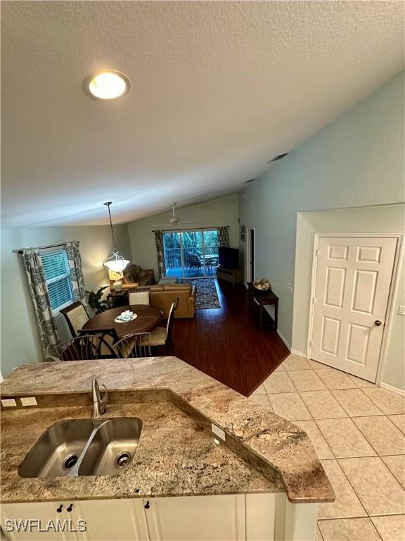 kitchen with vaulted ceiling, sink, decorative light fixtures, white cabinetry, and light tile patterned flooring