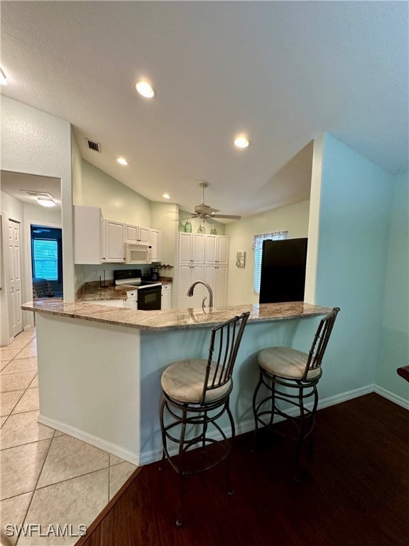 kitchen featuring black range oven, kitchen peninsula, light tile patterned floors, a kitchen bar, and white cabinetry