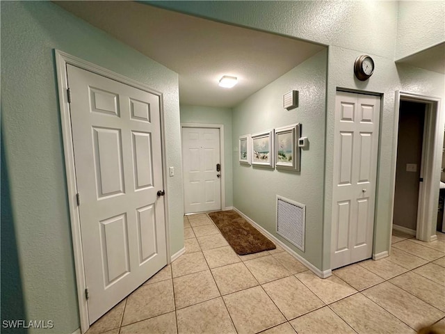 entryway featuring light tile patterned floors, a textured wall, visible vents, and baseboards