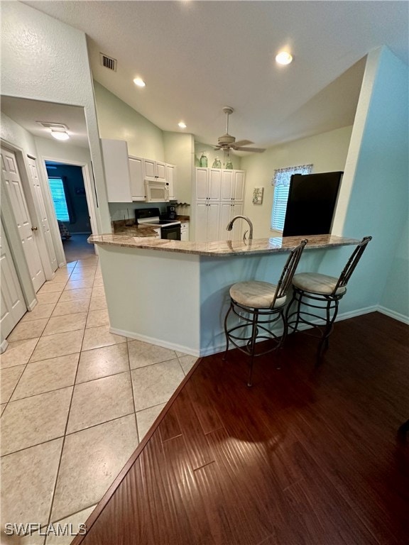 kitchen with white cabinets, a kitchen breakfast bar, black electric range, ceiling fan, and kitchen peninsula