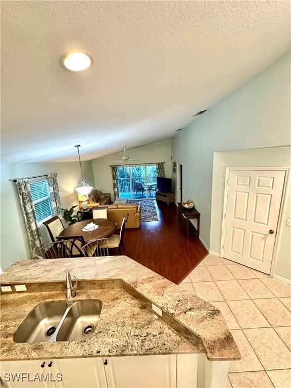 kitchen with sink, light tile patterned floors, white cabinets, hanging light fixtures, and lofted ceiling