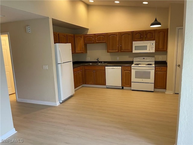 kitchen featuring white appliances, decorative light fixtures, a towering ceiling, and light wood-type flooring