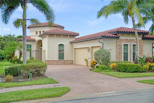 mediterranean / spanish-style home featuring a garage, stone siding, a tile roof, and stucco siding