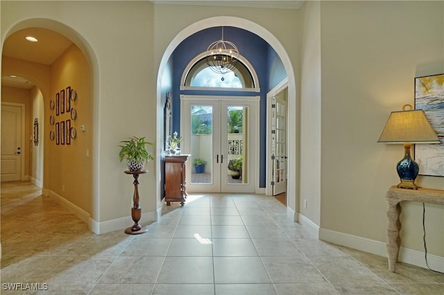 entryway with a chandelier, light tile patterned floors, arched walkways, baseboards, and french doors