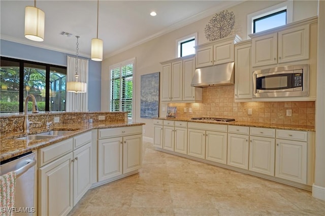 kitchen with cream cabinets, under cabinet range hood, a sink, hanging light fixtures, and appliances with stainless steel finishes