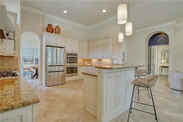 kitchen with arched walkways, hanging light fixtures, appliances with stainless steel finishes, and ventilation hood