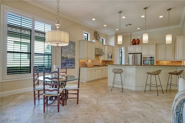 kitchen with a breakfast bar, stainless steel appliances, visible vents, ornamental molding, and under cabinet range hood