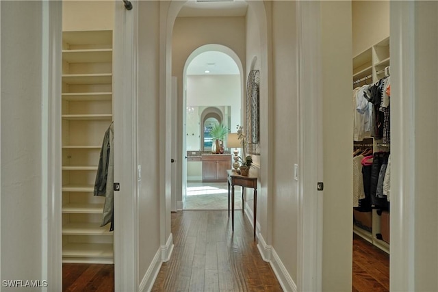 corridor with dark wood-style floors, arched walkways, and baseboards