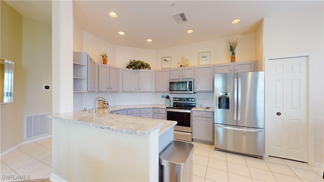 kitchen featuring tasteful backsplash, appliances with stainless steel finishes, light stone counters, kitchen peninsula, and light tile patterned flooring