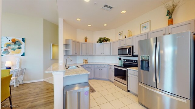 kitchen with light wood-type flooring, appliances with stainless steel finishes, light stone countertops, sink, and kitchen peninsula