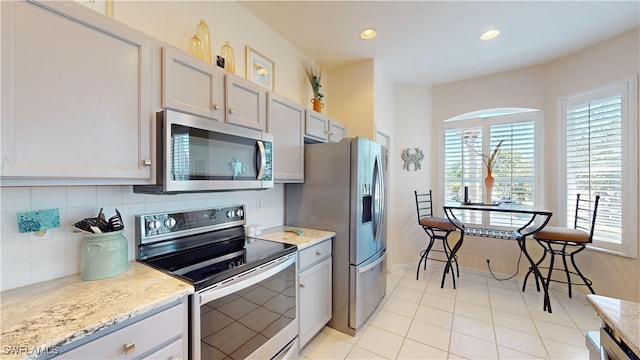 kitchen featuring stainless steel appliances, recessed lighting, decorative backsplash, and light stone countertops