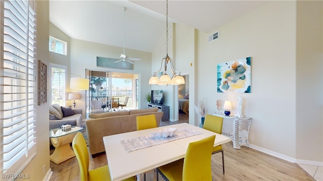 dining space featuring high vaulted ceiling, ceiling fan with notable chandelier, and light hardwood / wood-style floors