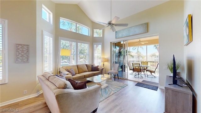 living room with a healthy amount of sunlight, light wood-style floors, baseboards, and high vaulted ceiling