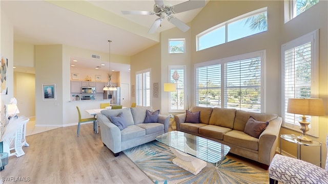 living room featuring a high ceiling, light hardwood / wood-style flooring, ceiling fan, and plenty of natural light