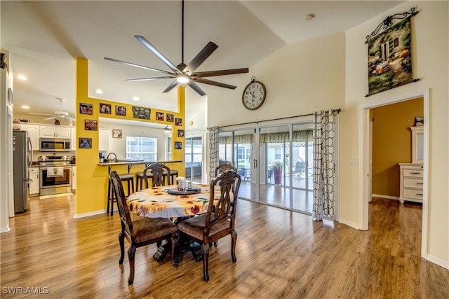 dining space with ceiling fan, light wood-type flooring, and high vaulted ceiling