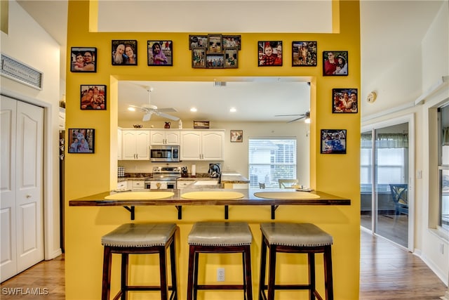 kitchen with appliances with stainless steel finishes, light wood-type flooring, a kitchen breakfast bar, kitchen peninsula, and ceiling fan