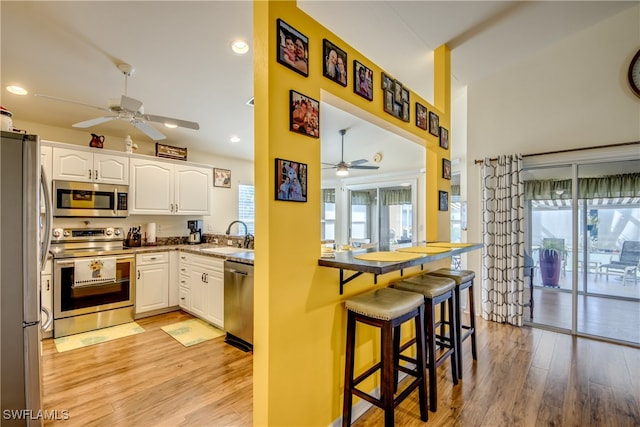 kitchen with light wood-type flooring, appliances with stainless steel finishes, ceiling fan, and white cabinets