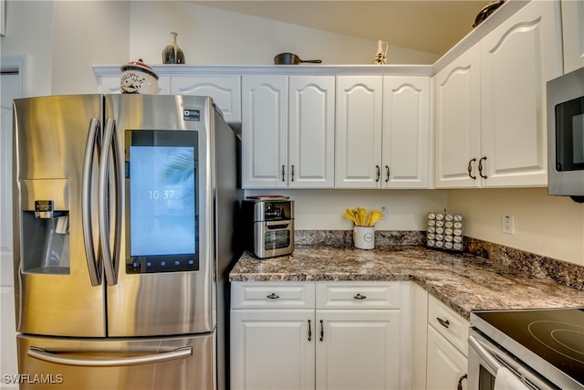 kitchen featuring white cabinetry, stainless steel refrigerator with ice dispenser, vaulted ceiling, dark stone countertops, and built in microwave