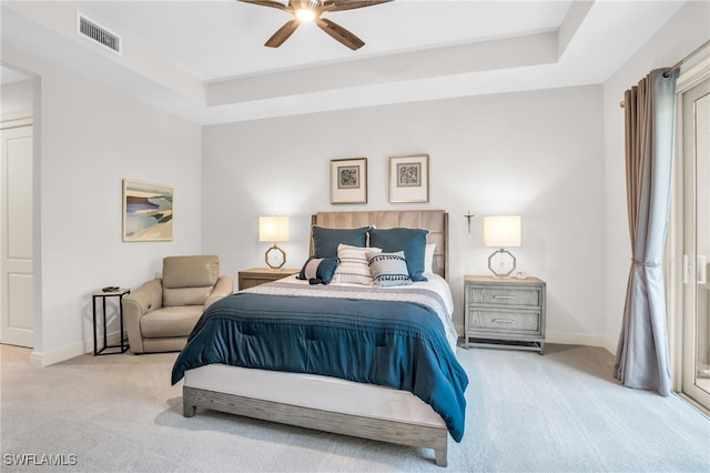 bedroom with ceiling fan, light carpet, and a tray ceiling