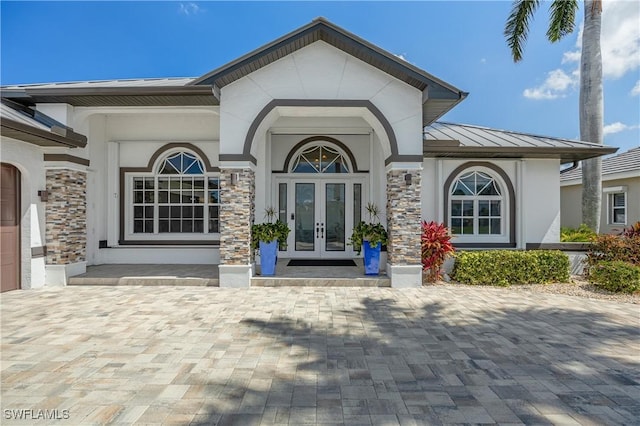 entrance to property with french doors, stucco siding, a standing seam roof, metal roof, and stone siding