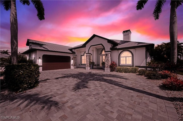 view of front facade featuring a garage, metal roof, decorative driveway, and stucco siding