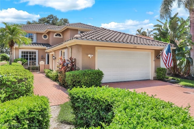 mediterranean / spanish home with decorative driveway, a tiled roof, an attached garage, and stucco siding