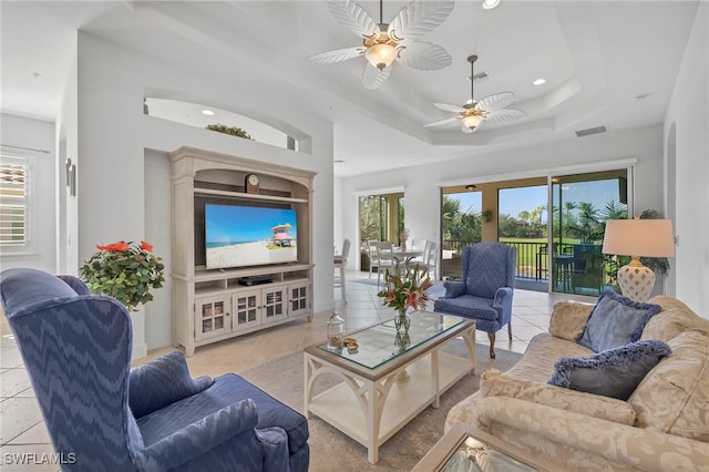 living room featuring ceiling fan, light tile patterned flooring, and a tray ceiling