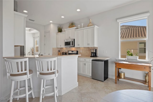 kitchen with white cabinetry, stainless steel appliances, a kitchen breakfast bar, kitchen peninsula, and decorative backsplash