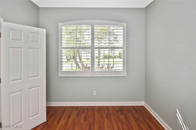 empty room with a wealth of natural light and dark hardwood / wood-style floors