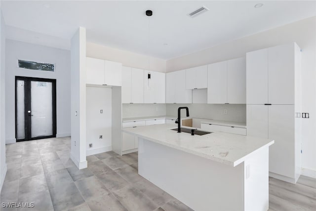 kitchen featuring pendant lighting, sink, white cabinetry, a center island with sink, and light stone countertops