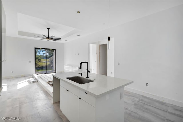 kitchen featuring ceiling fan, a raised ceiling, sink, a kitchen island with sink, and white cabinetry