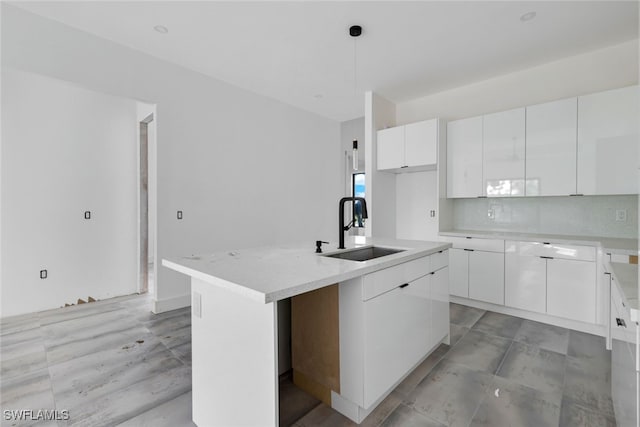 kitchen featuring sink, decorative light fixtures, a kitchen island with sink, white cabinetry, and decorative backsplash