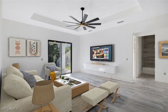 living area featuring a ceiling fan, a raised ceiling, visible vents, and baseboards