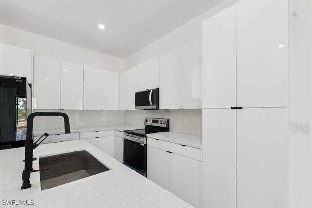 kitchen with decorative backsplash, appliances with stainless steel finishes, white cabinets, a sink, and modern cabinets