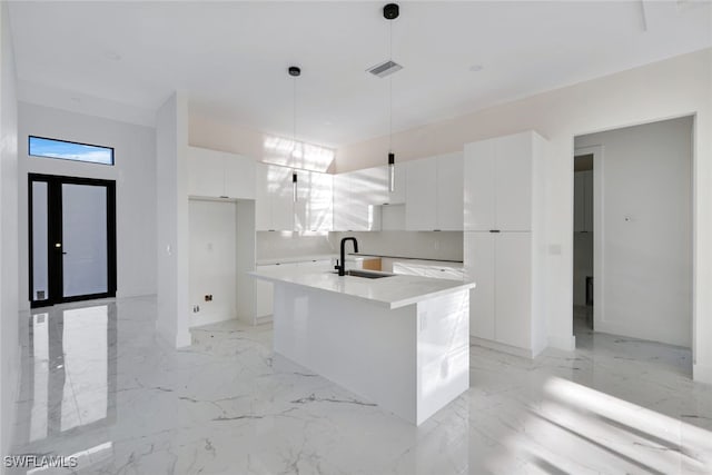 kitchen with hanging light fixtures, white cabinetry, sink, and an island with sink