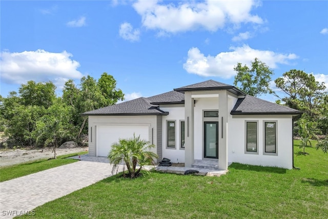 prairie-style home with a garage, roof with shingles, decorative driveway, a front yard, and stucco siding