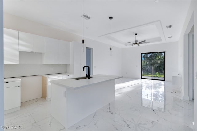 kitchen featuring pendant lighting, a tray ceiling, a kitchen island with sink, white cabinets, and ceiling fan