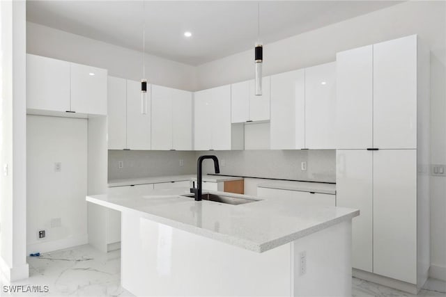 kitchen with marble finish floor, an island with sink, a sink, and white cabinets